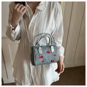 Elegant denim handbag with cherry embroidery worn by a model in a white summer dress