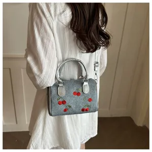 Detailed shot of denim crossbody bag with vibrant red cherry embroidery details.
