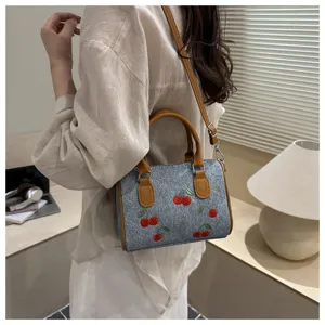 Model wearing a denim handbag with red cherry embroidery and tan leather handles