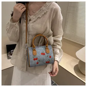 Detailed view of women's denim handbag with red cherry embroidery and brown handles