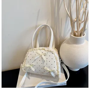 Elegante weiße gepunktete Handtasche mit Spitzenbesatz und Schleifen auf einem Buch.