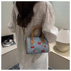 Detailed view of women's denim crossbody bag with embroidered cherry patterns and tan handles.