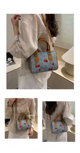 Detail view of cherry embroidered denim handbag with brown leather straps for women.