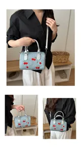 Close-up of stylish light blue denim handbag featuring vibrant red cherry embroidery details