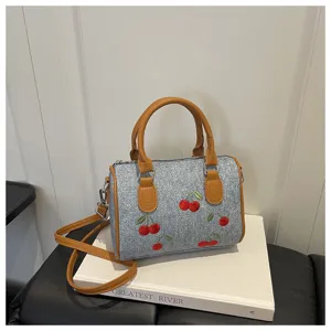 Detailed view of a denim handbag with red cherry embroidery set on a white book prop