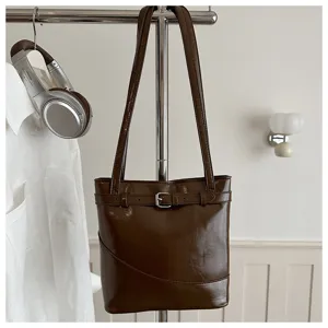 Elegante borsa a secchiello marrone scuro lucida con dettaglio cintura su rack cromato