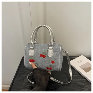 Detail view of denim barrel bag with red cherry embroidery and silver strap