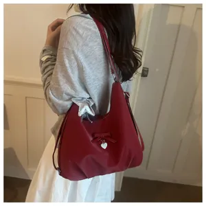 Large capacity red hobo shoulder bag with bow and heart charm detail shown on model.