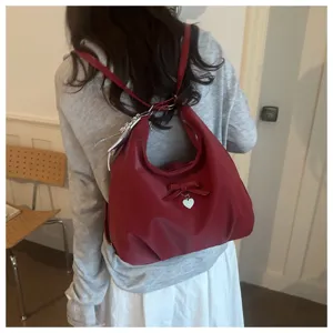 Detail of red bow hobo backpack worn as a shoulder bag by model in casual indoor setting.