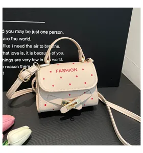 Close-up detail of a beige cream polka dot crossbody bag with gold belt buckle lock