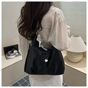 Detail of black large capacity shoulder bag with star charm worn by a model