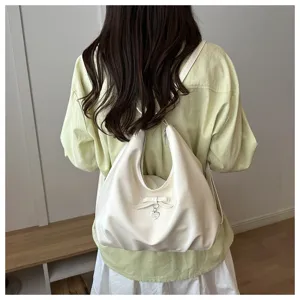 Versatile cream hobo bag worn as a backpack, featuring a cute bow and heart charm detail.