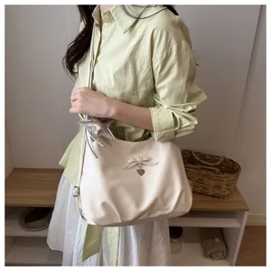 Close-up of cream white hobo bag with bow detail and star charm worn by a model