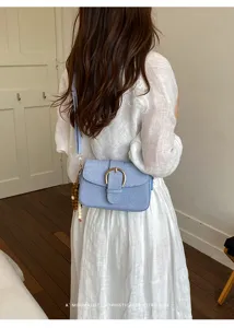 Close-up of minimalist light blue denim texture crossbody bag with gold horseshoe buckle