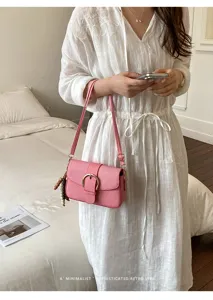 Pink textured small square bag with gold buckle on a minimalist white dress