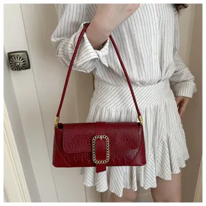Woman wearing a red crocodile-embossed baguette bag with a gold chain buckle detail.