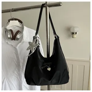 Detail of a minimalist black hobo shoulder bag with star and heart charms on a rack