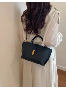 Elegante bolso de hombro en cuero negro con cierre de metal dorado en una modelo