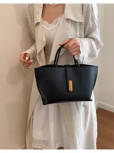 Modelo luciendo un elegante bolso cubo de cuero negro con un moderno cierre de hebilla dorada.