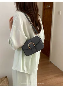 Back view of model wearing a black minimalist square crossbody bag with gold buckle.