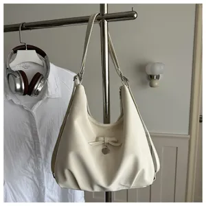 Detail view of a creamy white minimalist hobo bag with a decorative bow and heart charm