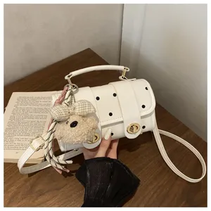 Close-up of a cute white polka dot crossbody pillow bag with a fluffy teddy bear charm