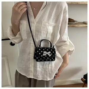 Gros plan d'une femme portant un mini sac bandoulière noir à pois avec un nœud strass