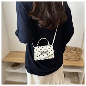 Vue détaillée d'un mini sac à pois blancs porté en bandoulière par un mannequin.