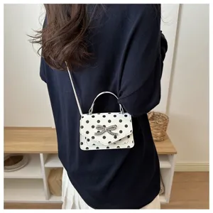 Détail d'un petit sac à bandoulière carré blanc à pois noirs avec un nœud argenté