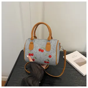 Close-up of denim handbag with detailed red cherry embroidery and leather handles
