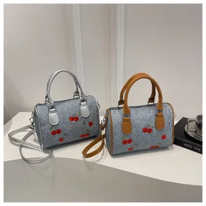 Detailed shot of cherry embroidered denim barrel bags with silver and tan handles