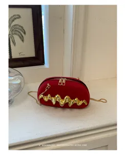 Dettaglio borsa da sera rossa con decorazione in metallo dorato ondulato e tracolla a catena.