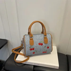 Stylish denim handbag with cherry embroidery and brown straps for summer fashion.