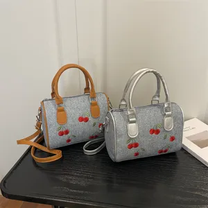 Chic denim barrel bags featuring red cherry embroidery, top handles, and adjustable straps