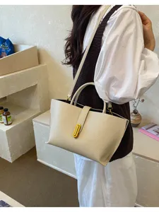 Vista detallada de un bolso tote de cuero crema con cierre dorado llevado por modelo