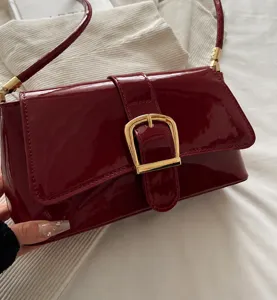 Close-up of red patent leather underarm bag featuring a prominent gold buckle detail
