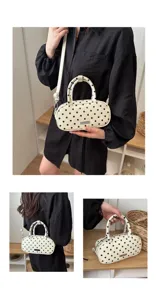 Detailed view of a white polka dot oval handbag shown held by hand and worn over shoulder