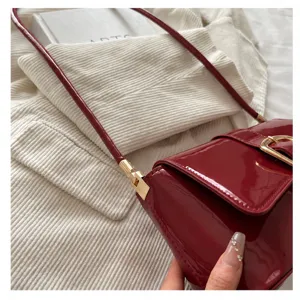 Close-up detail of a premium wine red patent leather handbag with a gold metal buckle