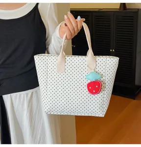 Close-up detail of white polka dot tote bag with a cute strawberry charm held by hand