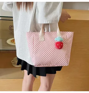 Detailed view of a pink polka dot tote bag with a cute strawberry charm accessory