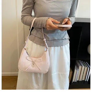 Détail d'un sac à nœud rose clair porté par un mannequin dans un décor doux.