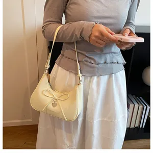 Gros plan d'un sac à bandoulière crème avec nœud et détail de breloque en cœur
