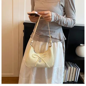 Gros plan d'un sac hobo élégant de couleur crème avec nœud et pendentif en cœur.