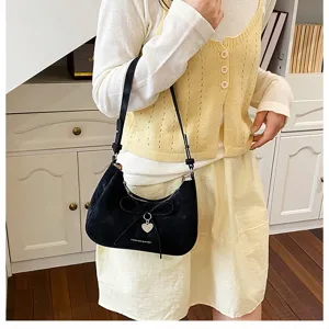 Détail d'un sac hobo noir avec nœud et breloque en cœur porté par un mannequin en tenue décontractée