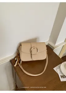 Minimalist beige textured crossbody bag featuring gold buckle and wooden bead tassel detail