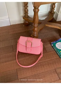 Minimalist retro pink shoulder bag with a golden buckle displayed on a wooden floor