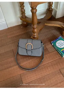 Retro minimalist textured small square crossbody bag with gold buckle on wooden floor.