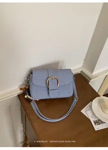 Close-up of a blue textured small square crossbody bag with a gold buckle on a wooden table