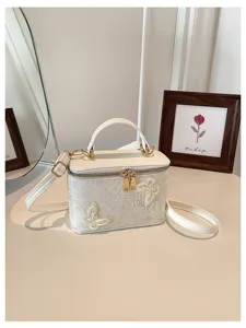 Dettaglio di un'elegante borsa a scatola in jacquard bianco con raffinato ricamo a farfalla.