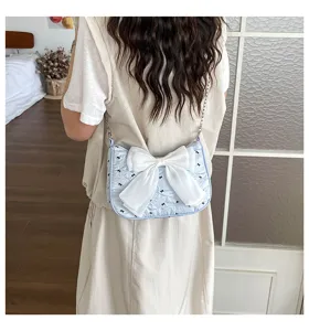 Back view of a light blue seersucker shoulder bag with a large white bow on a model